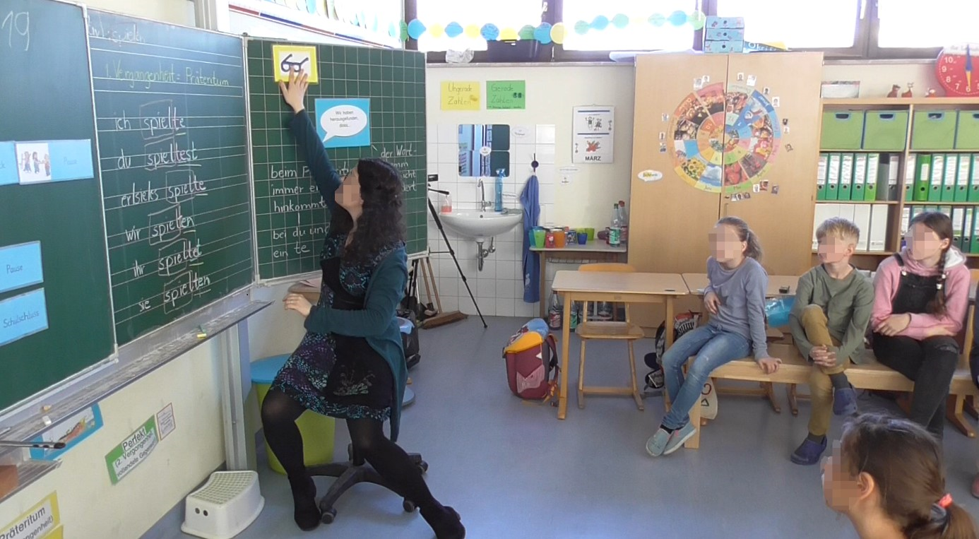 Sitzkreis der Schüler:innen mit Lehrerin vor der Tafel